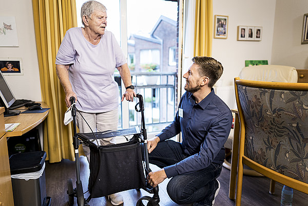 Situation im Pflegeheim: Eine alte Frau mit Gehhilfe und ein jüngerer Mann mit Namensschild im Gespräch